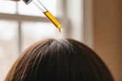 a dropper of oil above a scalp with brunette hair